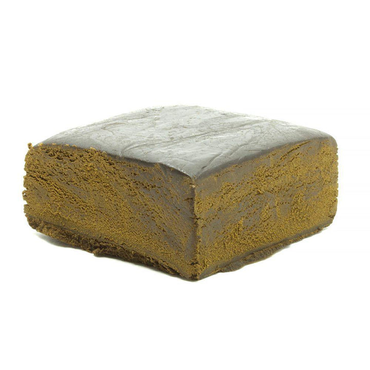A compact, solid block of CBD pollen hash with a textured surface, displaying a dark brown to black color, side view on a white background