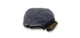 A black, solid-looking mass of CBD Squidgy Black Hash, resembling traditional black CBD hash.