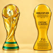 Cargar imagen en el visor de la galería, Two gold FIFA World Cup trophy-shaped bottles for Fortune Flavours, shown side by side against a warm beige background. The left bottle displays the front design resembling the World Cup trophy with a globe and player silhouette, while the right bottle shows the back with text including 'WORLD CUP #26' and 'FORTUNE FLAVOURS'.
